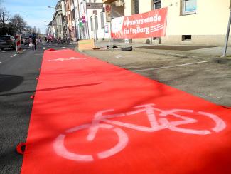 Roter Teppich mit weißem Fahrradsymbol im Hintergrund ein Banner mit der Aufschrift Verkehrswende für Freiburg