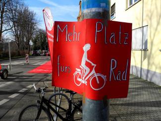 Rotes Schild mit der Aufschrift "mehr Platz fürs Rad", im Hintergund Roter Teppich