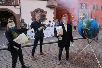 Drei Menschen mit Masken stehen neben brennendem Globus aus Pappmarché