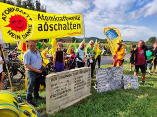 Menschen demonstrieren vor einem Gedenkstein gegen Atomkraft