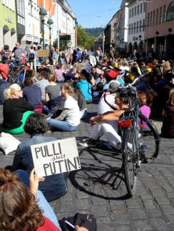 Schild "Pulli statt Putin". Im Hintergrund sitzen Menschen auf dem Platz am Bertholtsbrunnen.