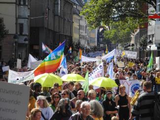 Menschenmenge mit Bannern, Regenschirmen und PEACE-Flagge