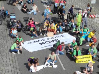 Menschen sitzen auf der Straße. Auf dem Boden liegt ein Banner "Climate Justice Now"