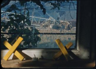 Das Bild zeigt eine Szene aus dem Kurzfilm "Hang am Baum": abgebilded ist der Blick aus einem Fenster auf einen riesigen Schaufelradbagger im Tagebau. Auf der Fensterbank sind zwei gelbe Holzkreuze zu sehen – das weithin bekannte Symbol der Klimaschutz- und Protestbewegung „Lützerath bleibt“.